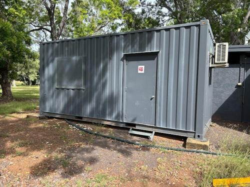 a small gray shed with a door in a yard at Territory Manor Motel & Caravan Park in Mataranka