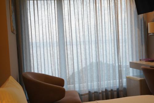 a room with a window with white curtains and a chair at Bougainville Bay Hotel in Sarandë