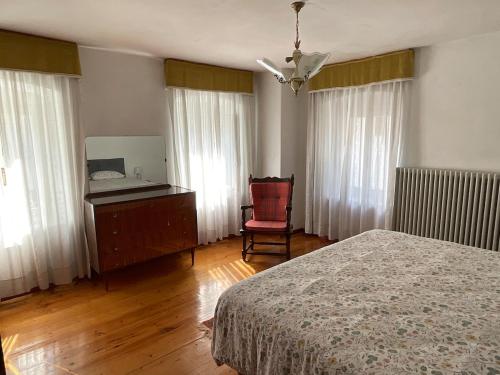 ein Schlafzimmer mit einem Bett und einem Stuhl und Fenstern in der Unterkunft Ciasa Larese, between the lake and the Dolomites in Auronzo di Cadore
