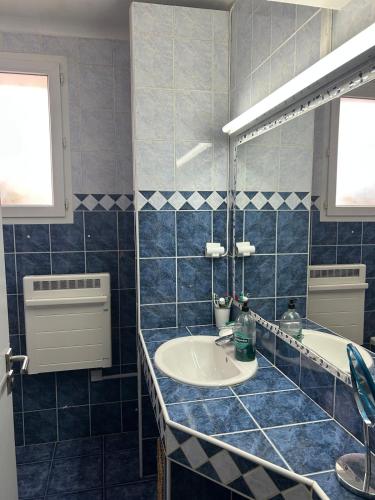 La salle de bains est pourvue de carrelage bleu, d'un lavabo et d'un miroir. dans l'établissement Cozy apartment with parking 5 min from downtown, à Aix-en-Provence