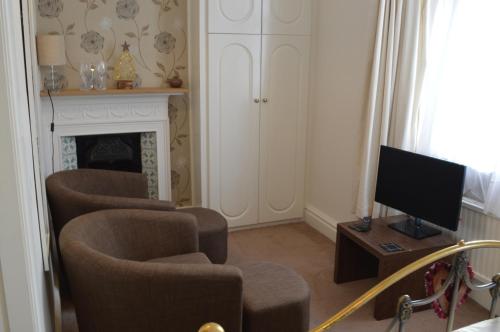 a living room with chairs and a tv and a fireplace at Ellerbrook House in Windermere