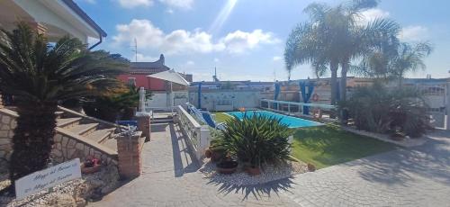 a swimming pool with palm trees in front of a building at Alloggi Turistici con Piscina Palestra Jacuzzi Sauna - All Inclusive in Anzio