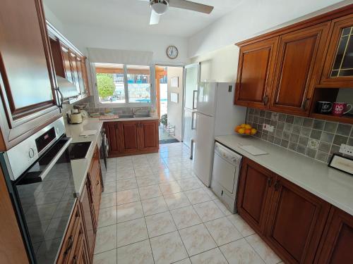 a kitchen with wooden cabinets and a white refrigerator at Villa Best Holiday- breathtaking sea views, amazing garden, private pool, BBQ, next to CORAL BAY, Lower Peyia, Paphos in Peyia