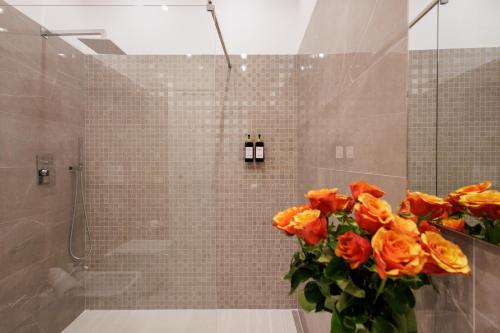 a bathroom with a shower with a vase of orange roses at Genoa Lux Apartments with parking in Genova