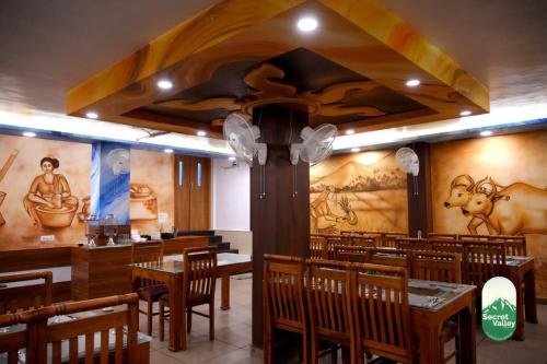 a restaurant with wooden tables and chairs and paintings on the walls at Secret Valley Planation Resort in Munnar
