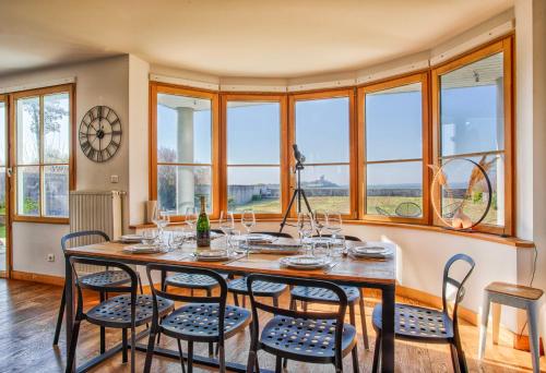 une salle à manger avec une table, des chaises et des fenêtres dans l'établissement Gîte La Ligne Bleue front de mer et vue sur une Tour Vauban, à Saint-Vaast-la-Hougue