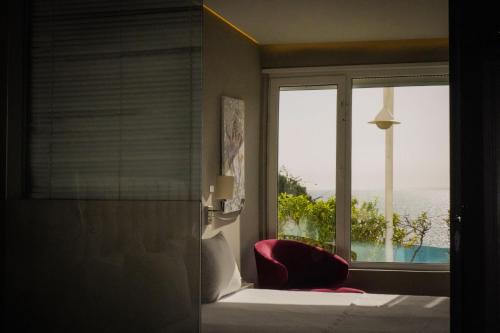 a bedroom with a window and a bed and a red chair at Bougainville Bay Hotel in Sarandë