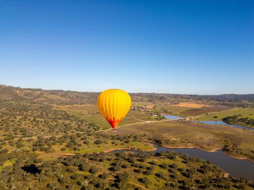 a yellow hot air balloon flying over a river at Herdade Do Sobroso Wine & Luxury Boutique Hotel in Pedrógão
