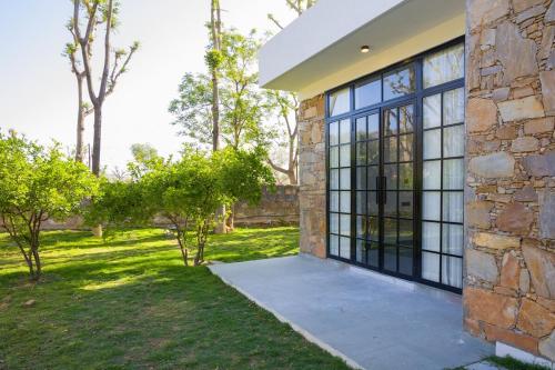 a stone house with black windows and a yard at Nature 95 by ELIVAAS 4 BHK Farm with Private Pool in Chandwaji