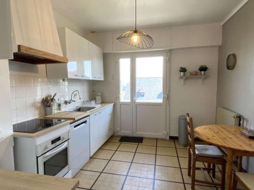 une cuisine avec des armoires blanches, une table et une fenêtre dans l'établissement Maison à 550m de la plage avec jardin, balcon et Wi-Fi à Perros-Guirec - FR-1-368-433, à Perros-Guirec