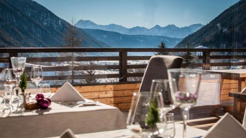 two tables with wine glasses on a balcony with mountains at La Casies Mountain Hotel in Santa Maddalena in Casies