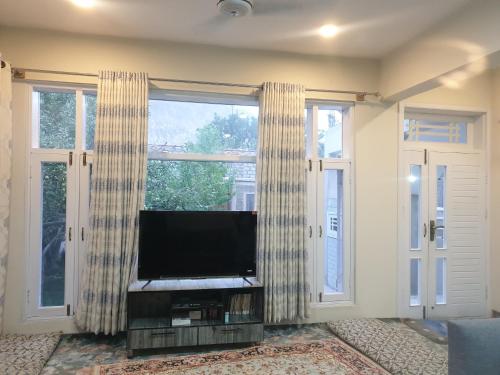 a living room with a flat screen tv and two windows at Mountain Villa - Hunza Valley in Hunza