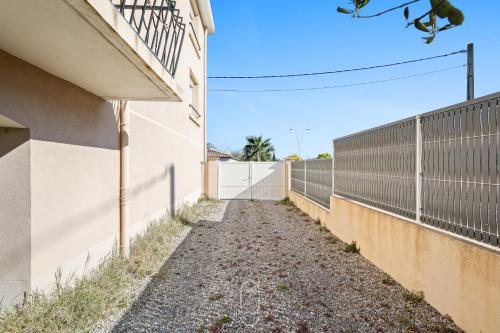 une allée entre une clôture et un bâtiment dans l'établissement Appartement 3 étoiles coquet à 700m de la mer Les Bonnettes WiFi PK BY HC, au Pradet