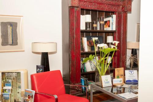 a red chair and a book shelf with books at Hotel Arbe in Mutriku
