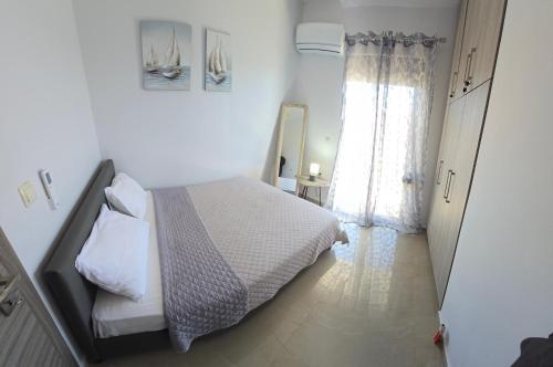 a white bedroom with a bed and a window at Odyssea Seaside Apartment with Sea View and Pool in Kremasti