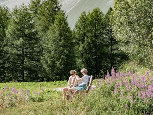 two people sitting on a bench in a field of flowers at Hotel Chesa Pool in Sils Maria