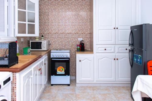 a kitchen with white cabinets and a black refrigerator at Le Rooftop Apparte - Barbecue, Grande Terrasse in Nabeul