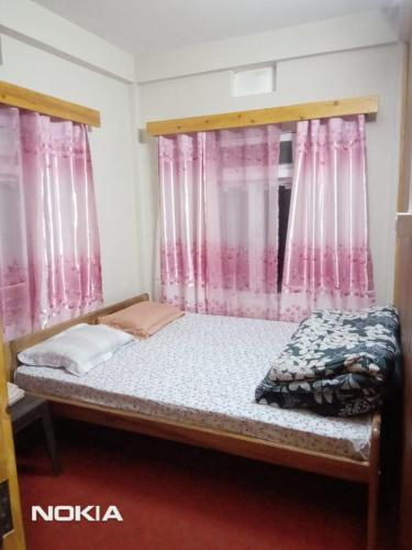 a bed in a room with pink curtains at Yellow Bamboo Homestay in Mangpu