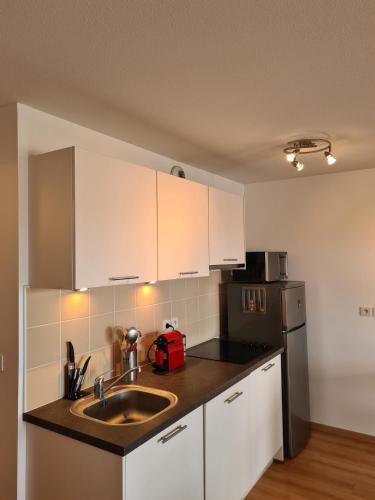 une cuisine avec des armoires blanches, un évier et un réfrigérateur dans l'établissement Appartement a 50m de la plage, à Biscarrosse