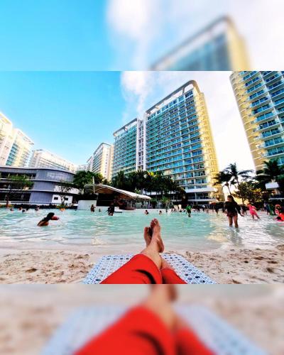 a person laying on a beach with people in the water at Cozy 1BR with City View, Beach Access and Wave Pool in Manila