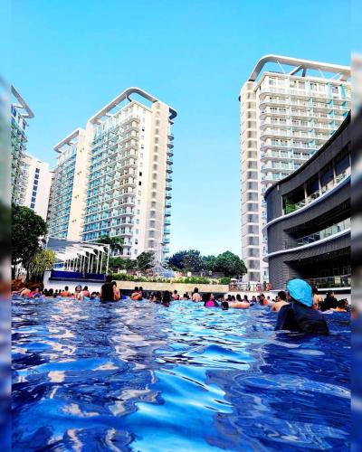 a group of people swimming in a pool with tall buildings at Cozy 1BR with City View, Beach Access and Wave Pool in Manila