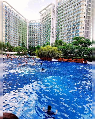 people swimming in a swimming pool in front of buildings at Cozy 1BR with City View, Beach Access and Wave Pool in Manila