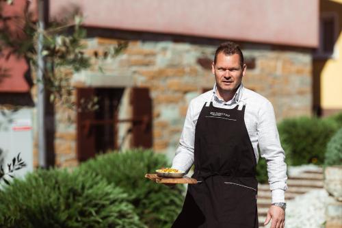a man in an apron holding a plate of food at TouristFarm - apartments "RED FAIRYTALE" in Marezige