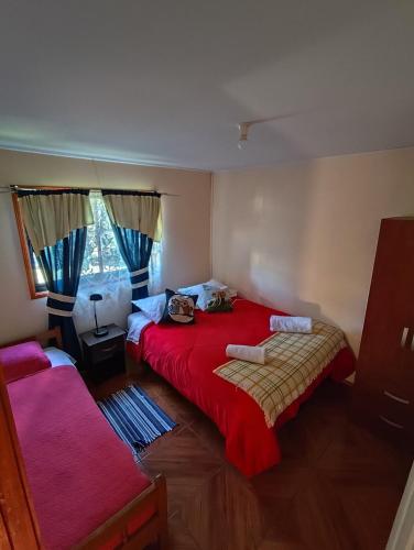 a bedroom with a red bed and a window at Cabaña camino Conguillio Sector Urbano in Melipeuco