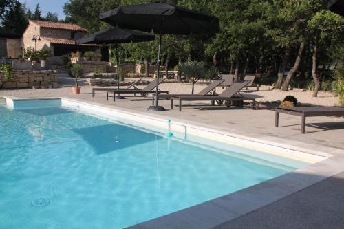 a swimming pool with chairs and umbrellas next to it at Les Chambres du Hameau in Gordes