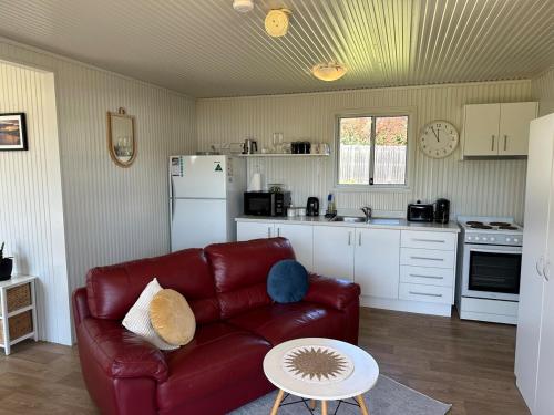 a living room with a red couch and a kitchen at Cabin Bellbird in Bermagui
