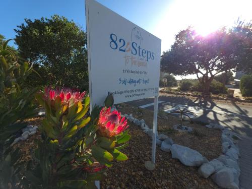 a sign with pink flowers in front of a garden at 82 Steps to the Beach in Pringle Bay