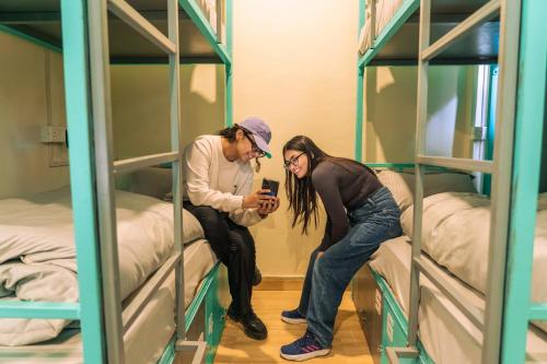a man and woman looking at a cell phone in a bunk bed at Traverse Hostel Kasol in Kasol