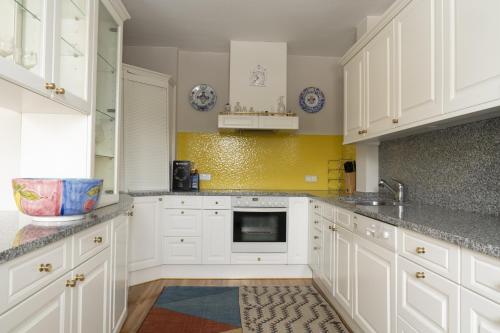 a kitchen with white cabinets and a yellow wall at Landhaus zum Caphenstain in Gutendorf