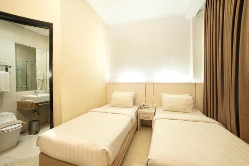 two beds in a hotel room with a bathroom at Ros-In Hotel in Yogyakarta