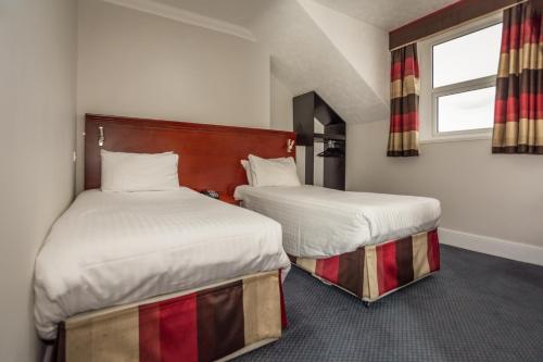 two beds in a hotel room with a window at Kensington Hotel in Llandudno