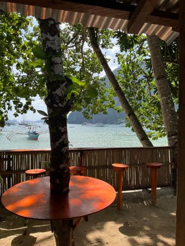 a table with a tree in front of the water at Rosies Beach House El Nido in El Nido