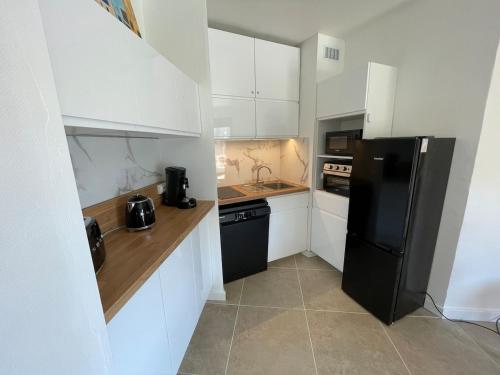 une cuisine avec des armoires blanches et un réfrigérateur noir dans l'établissement T2 idéal à 50m de la plage Tout à pied Parfait pour des vacances relax, à Cavalaire-sur-Mer
