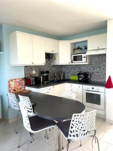 une cuisine avec des armoires blanches et une table et des chaises dans l'établissement Appartement face à la mer, à Guidel