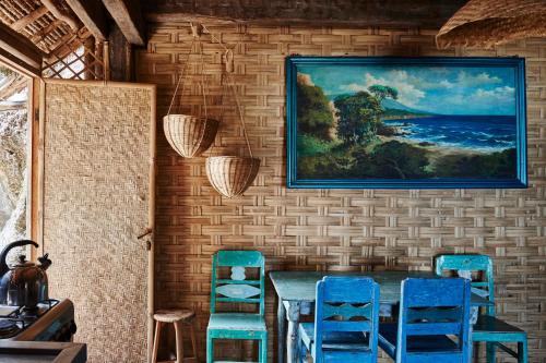 a dining room with blue chairs and a painting on the wall at The Island Houses Bingin in Uluwatu