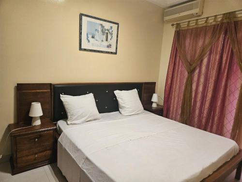 a bedroom with a bed with white sheets and a window at Keur Aïda Immeuble de standing in Dakar