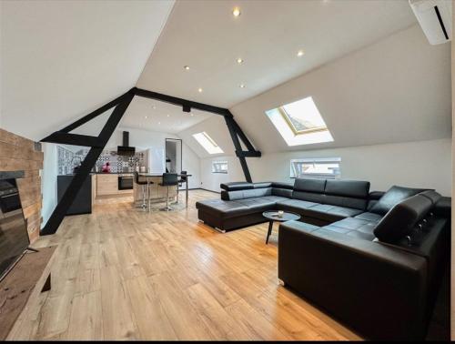 un salon avec un canapé noir et une cuisine dans l'établissement Ô13 Loft privatif sauna balnéothérapie à 30min de Pairi Daiza, à Quiévrechain