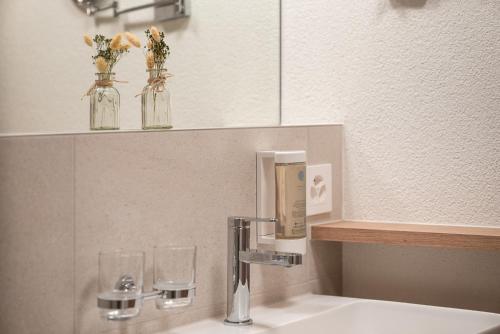 a bathroom sink with a faucet and two glass jars with flowers at Hotel-Restaurant Seegarten-Marina in Spiez