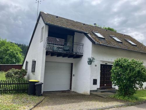 a white house with a garage and a balcony at Ferienhaus am Mühlenberg in Schleiden