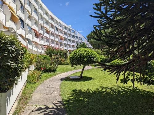 a building with a tree in the grass next to a sidewalk at Appartement Cabine - Résidence du PARC - Quartier du couchant - Proche de la mer in La Grande-Motte