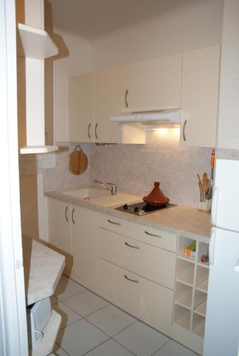La cuisine blanche est équipée d'un évier et d'un réfrigérateur blanc. dans l'établissement Face mer, grand studio de 32m2, clim, wifi, parking, proche commerces, à Saint Cyprien Plage