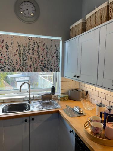a kitchen with a sink and a window with a clock at The Dairy Flat in Cheddar
