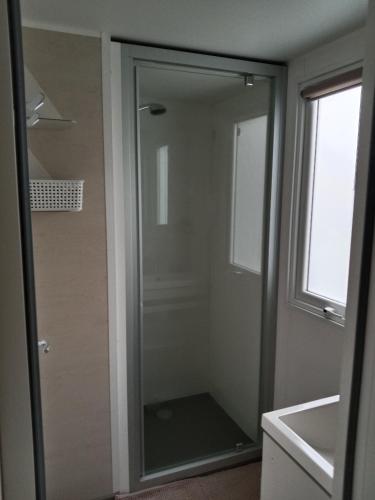 La salle de bains est pourvue d'un lavabo et d'une porte de douche en verre. dans l'établissement Mobile home SUPER CORDELIA CONFORT & FAMILIAL, à Pont-Aven