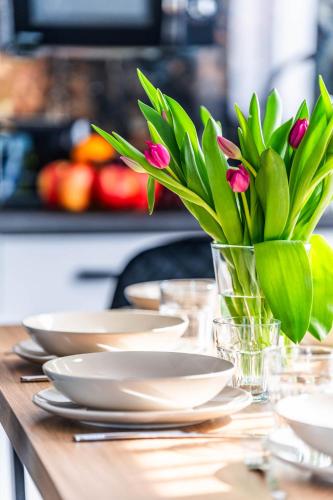 a table with white plates and a vase with pink flowers at Top Alex domki Międzyzdroje Lubin in Międzyzdroje