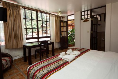 a bedroom with a bed and a desk and windows at Gringo Bill's Boutique Hotel in Machu Picchu