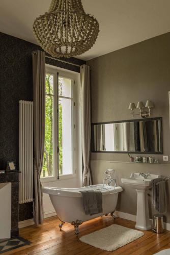 une salle de bain avec une baignoire, un lavabo et un lustre dans l'établissement Chateau Mathias, à Virazeil